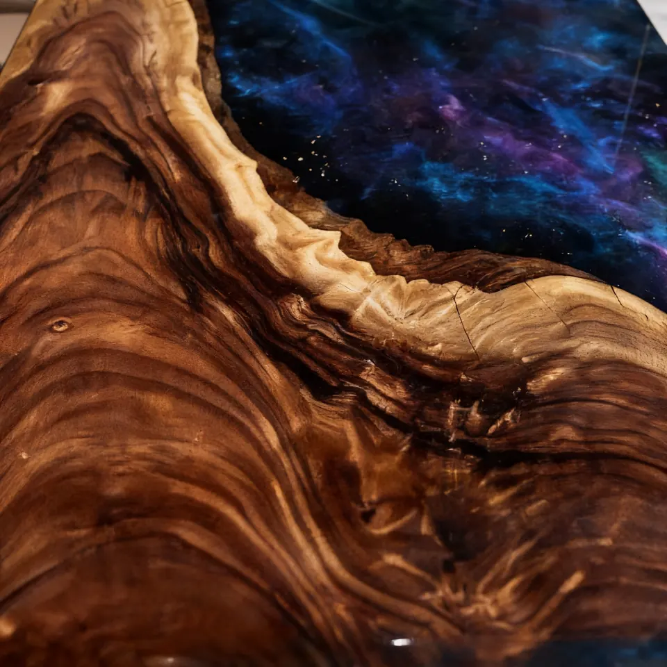 A close macro study of walnut grain flowing beside a deep starlit-blue resin channel